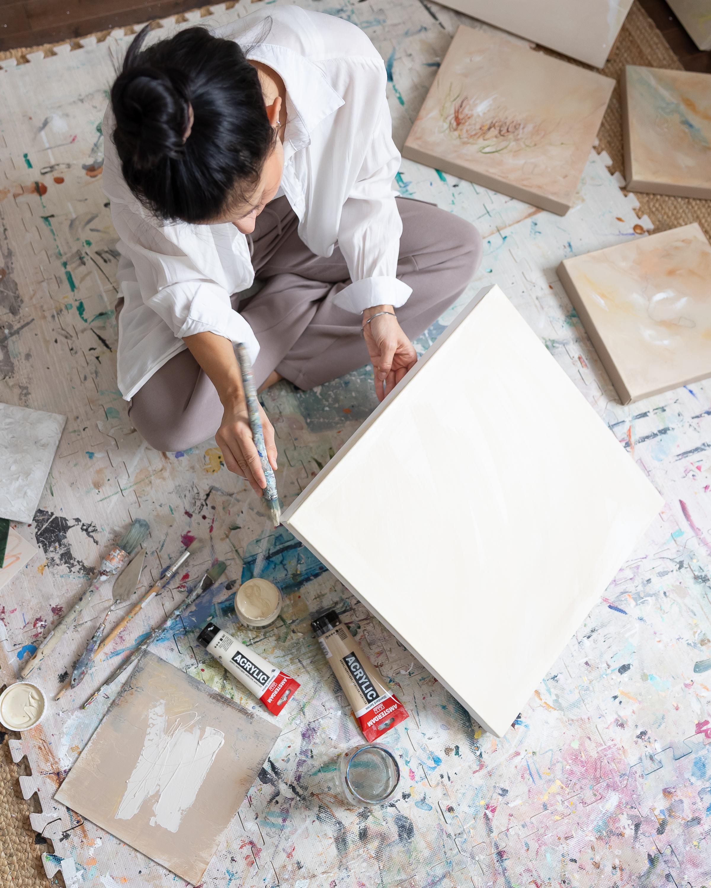 Artiste peignant une toile abstraite à l'acrylique, entourée d'œuvres et de pinceaux.