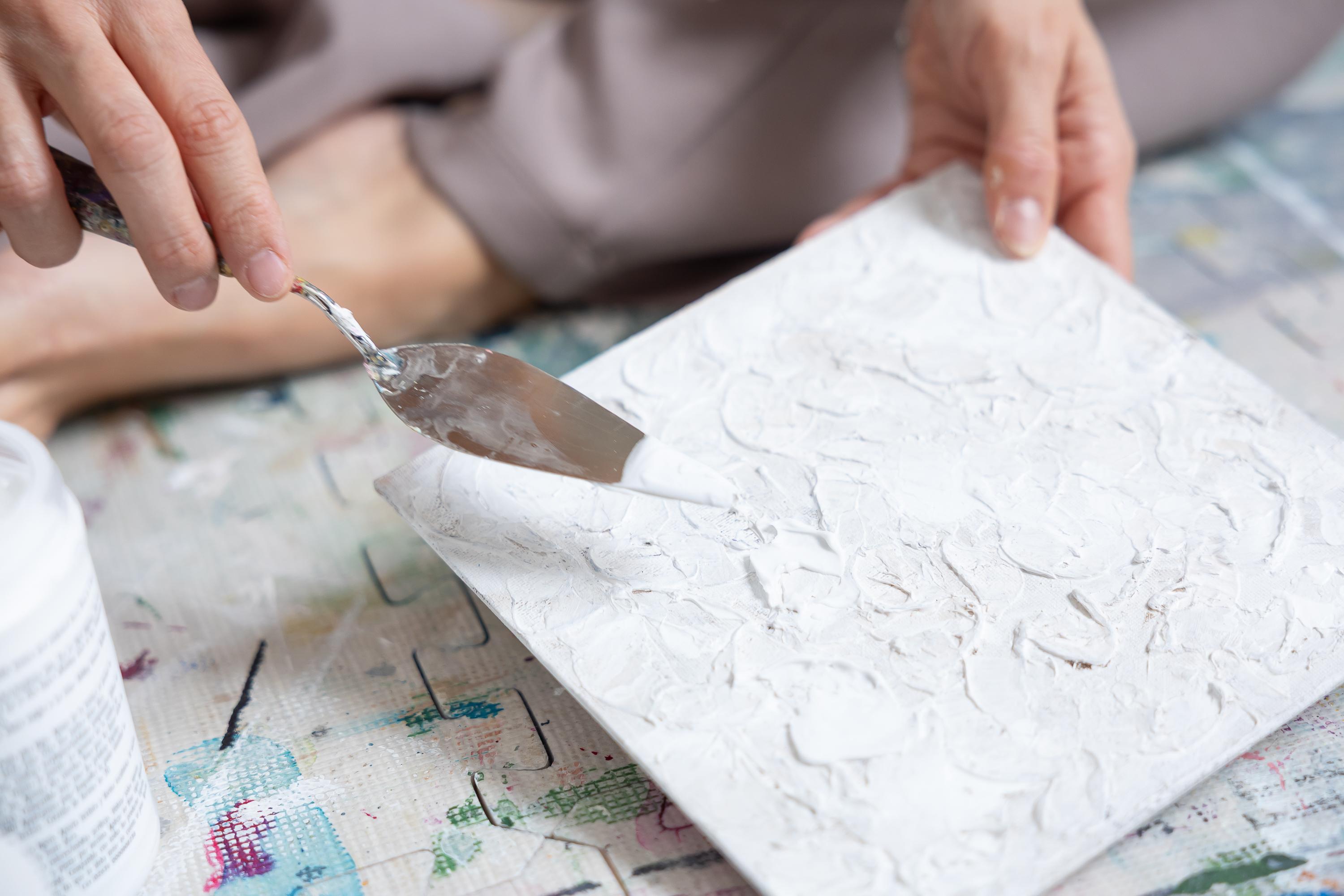 Main appliquant de la texture blanche sur une toile abstraite avec un couteau à peindre